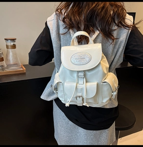 Détail du sac à dos en cuir blanc brillant avec plaque logo et poches à boucles