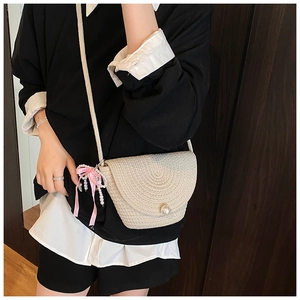 Detail of a woven straw crossbody bag with pearl button and pink bow charm