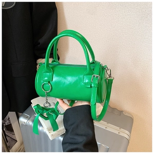Detail of green cylinder handbag featuring silk bow charm and shiny synthetic leather