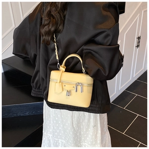 Detail of a bright yellow vanity bag with lychee texture and silver rivets on a model