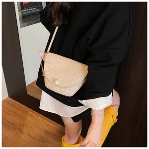 Detail of hand-woven straw crossbody bag with large pearl clasp and pink bow accessory