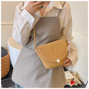 Detail of beige straw crossbody bag with large pearl button and woven texture