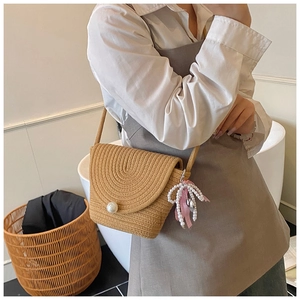 Detail of woven beige crossbody bag with large pearl buckle and pink ribbon bow pendant