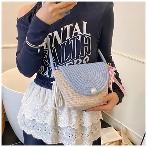 Detail view of woven straw crossbody bag with blue circular pattern and pearl closure