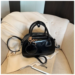 Vue détaillée d'un sac à main en cuir verni noir avec surpiqûres blanches et charme rond