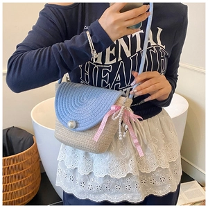 Detail of blue and beige woven crossbody bag featuring a large pearl clasp and bow charm
