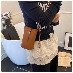 Détail d'un sac bandoulière en cuir marron avec boucle en fer à cheval et breloque en cœur