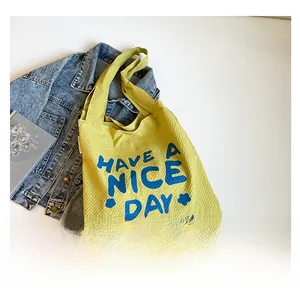 Vue à plat d'un sac cabas en toile jaune gaufrée avec lettrage bleu et décor en denim