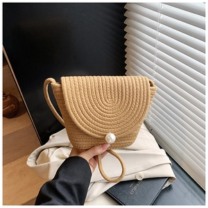 Close-up of woven straw handbag featuring a large pearl clasp and delicate shoulder strap