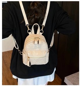 Détail du sac à dos crème avec motifs trèfle et fermetures éclair dorées sur le dos