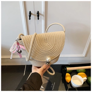 Close-up of beige woven crossbody bag with pearl buckle and decorative ribbon charm