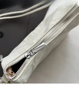 Detail view of the silver metal zipper and marble-textured pleated fabric on a beige handbag