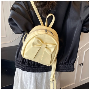 Detailed back view of a mini yellow backpack with a large bow on a stylish female model