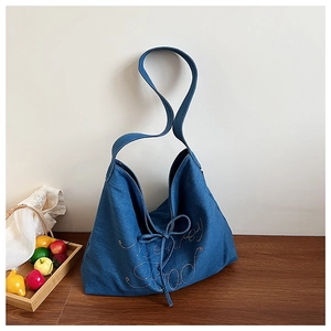 Detail of blue denim tote bag featuring sparkly cursive lettering and drawstring closure