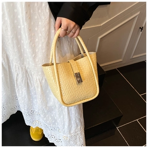 Detail of light yellow woven texture bucket bag with silver metal lock closure