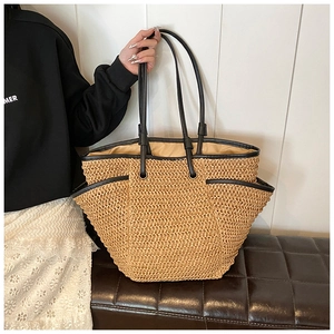 Detail of a beige woven straw tote with black leather trim and side storage pocket