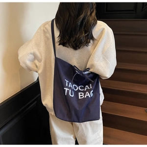 Model wearing a navy blue canvas tote bag with white lettering on a stylish shoulder strap
