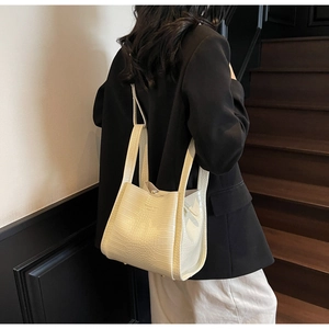 Détail d'un sac seau blanc cassé à effet croco porté avec un blazer noir sophistiqué
