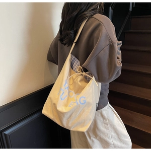 Close-up of beige canvas tote bag with light blue lettering and checkered drawstring