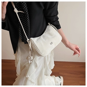 Close-up of cream-white half-moon shoulder bag with a metal logo and cloud charm detail