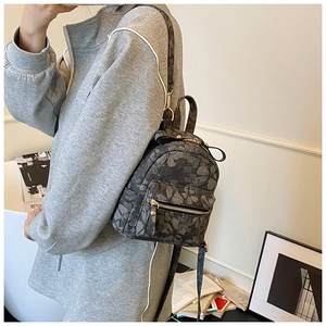 Détail d'un mini sac à dos gris à motif floral avec fermetures dorées et bretelles
