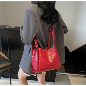 Sac seau rouge à texture crocodile présenté dans un décor lifestyle avec un tailleur gris