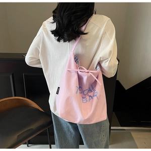 Pink canvas tote bag shown as a crossbody view on a model in a warm indoor setting