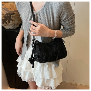 Detail view of black pleated dumpling bag with cute cat pendant and shoulder strap