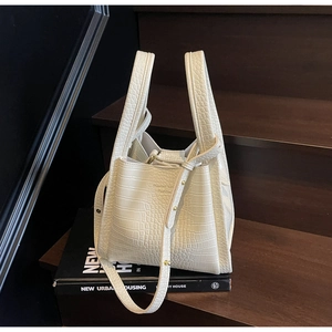 Détail du sac seau blanc cassé avec texture crocodile posé sur un livre
