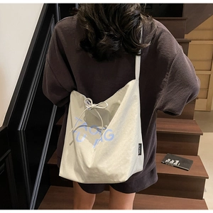 Detail view of large beige canvas tote bag featuring blue letters and a drawstring closure