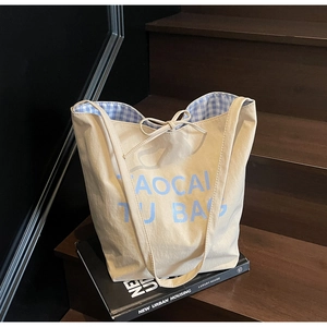 Close-up of beige canvas tote bag featuring blue letter print and check lining detail