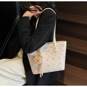 Detail of a chic cream tote bag with reindeer print and a brown plush bear charm accessory