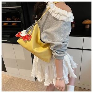 Detail of bright yellow leather tote bag with silver chain and red elephant charm