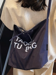 Large navy canvas tote bag with white lettering and bow detail shown on shoulder