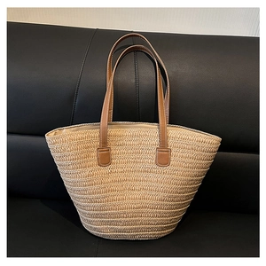 Detail of woven straw tote bag with brown leather handles and white contrast stitching