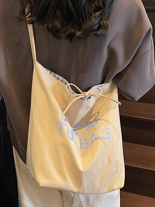 Minimalist beige canvas tote bag with blue TUCAN lettering and gingham lining shown on model