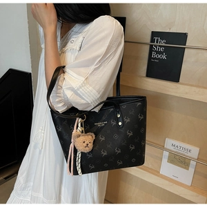 Detail of black patterned tote bag with plush bear charm worn with white dress
