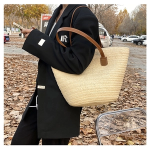 Detail shot of woven straw tote bag featuring brown leather straps and natural texture