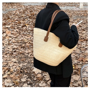 Macro detail of straw woven tote bag featuring brown leather shoulder straps on autumn leaves