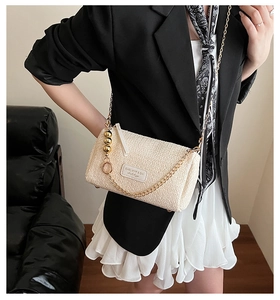 Détail du sac bandoulière beige texturé avec chaîne dorée et breloques boules dorées