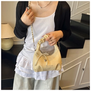 Detail of beige pleated cloud bag with pearl bow charm and chain strap on a model