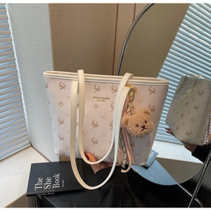 Close-up of beige tote bag with brown deer monogram pattern and plush bear charm