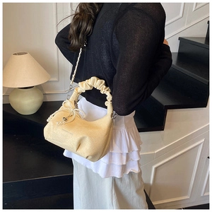 Close-up of pleated beige cloud bag with pearl bow pendant and textured wave handle