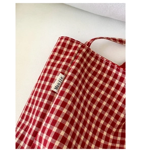 Detail of red gingham canvas tote fabric with neat stitching and woven logo label