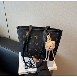Detail of black tote bag with deer pattern and decorative bear charm hanging on the strap