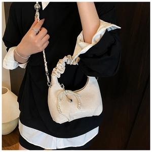 Close-up of beige ruched handbag featuring pearl bow detail and braided chain strap