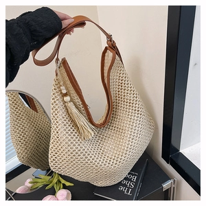Détail d'un sac hobo en paille tressée beige avec finitions en cuir marron et glands