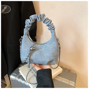 Detail of light blue denim croissant bag featuring ruched handle and metal ball charm