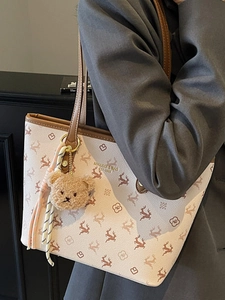 Chic beige leather tote bag with elk patterns and plush bear charm shown on model shoulder