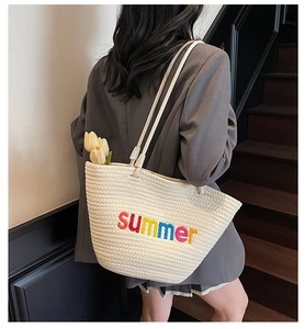 Detail of handwoven cream straw tote bag featuring colorful summer embroidery letters